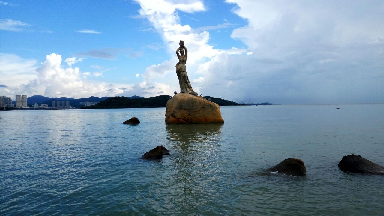 ·珠海渔女像位于香炉湾畔,由中国著名雕塑家潘鹤制作,雕像身高约8.7米,由70余块花岗岩打造,是珠海的标志性景观。
·渔女领戴项珠,身掮渔网,裤脚轻挽,双手高高擎举一颗晶莹璀璨的珍珠,带着喜悦而又含羞的神情,向世界昭示着光明。
·珠海本身有一个传说,远古时代有位仙女被香炉湾风光迷住,扮成渔女下凡,与渔民海鹏私定终身,但海鹏听信谗言,导致渔女死去。九洲长老为这深情所感动,救活了仙女,从此仙女成了真正的渔女。成亲当日,渔女把她挖到的一颗