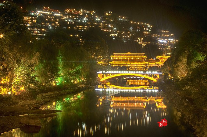 风雨桥和山上璀璨的灯光倒映在河里,这就是苗寨的夜色.