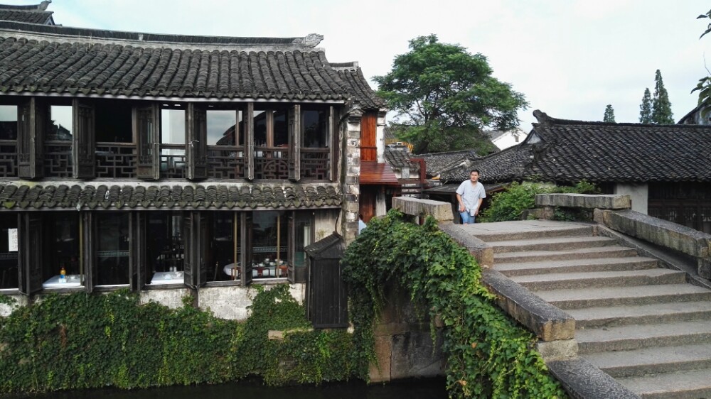 在周庄双桥,上海旅美画家陈逸飞创作出《故乡的回忆》,成为联合国首日封的图案,自此,养在深闺人未识的周庄开始走进大众视野。
一天的生活,从桥上开始。带着妹妹,从清晨,走过没有游人的双桥,便开始在周庄漫游。没有特定的目的,走走停停,一遍又一遍,发现着自己的周庄。漫步于双桥,阿婆们在河边开始了一天的生活,驻扎在周庄的画家,也开始了一天的创作。不时,还会有路过的阿姨用地道的周庄话向你问好,一声早啊像一阵暖流,注入心间,暖暖的,让我忘记了所有林立的店铺,回到了最初的周庄。
